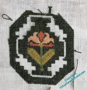 Tudor style design of a honeysuckle sprig surrounded by dark green tent stitch. There are furry bits of unpicking and knots of thread starting all around, and the green isn't yet all in place.