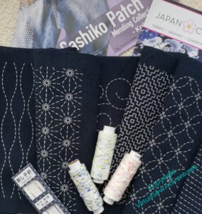 The contents of my Christmastide Diversions kit - a navy blue panel marked in Sashiko patterns, some sashiko thread and needles