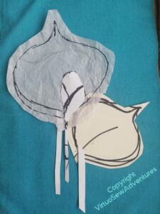 Cut outs of leaves and a bud, lying on the tweed fabric of the coat