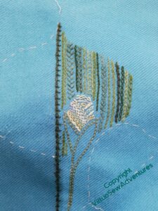 One half leaf and the bud stitched, again in rows of chain and feather stitch variations, The bud is very pale greens against the darker leaf behind.